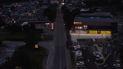 Los-Reenvíos-Vuelan-Por-Encima-De-La-Carretera-En-Los-Suburbios.-Inclínate-Hacia-Arriba-Para-Revelar-La-Ciudad-Al-Anochecer.-Poco-Tráfico-En-Las-Calles-De-La-Noche.-Killarney,-Irlanda