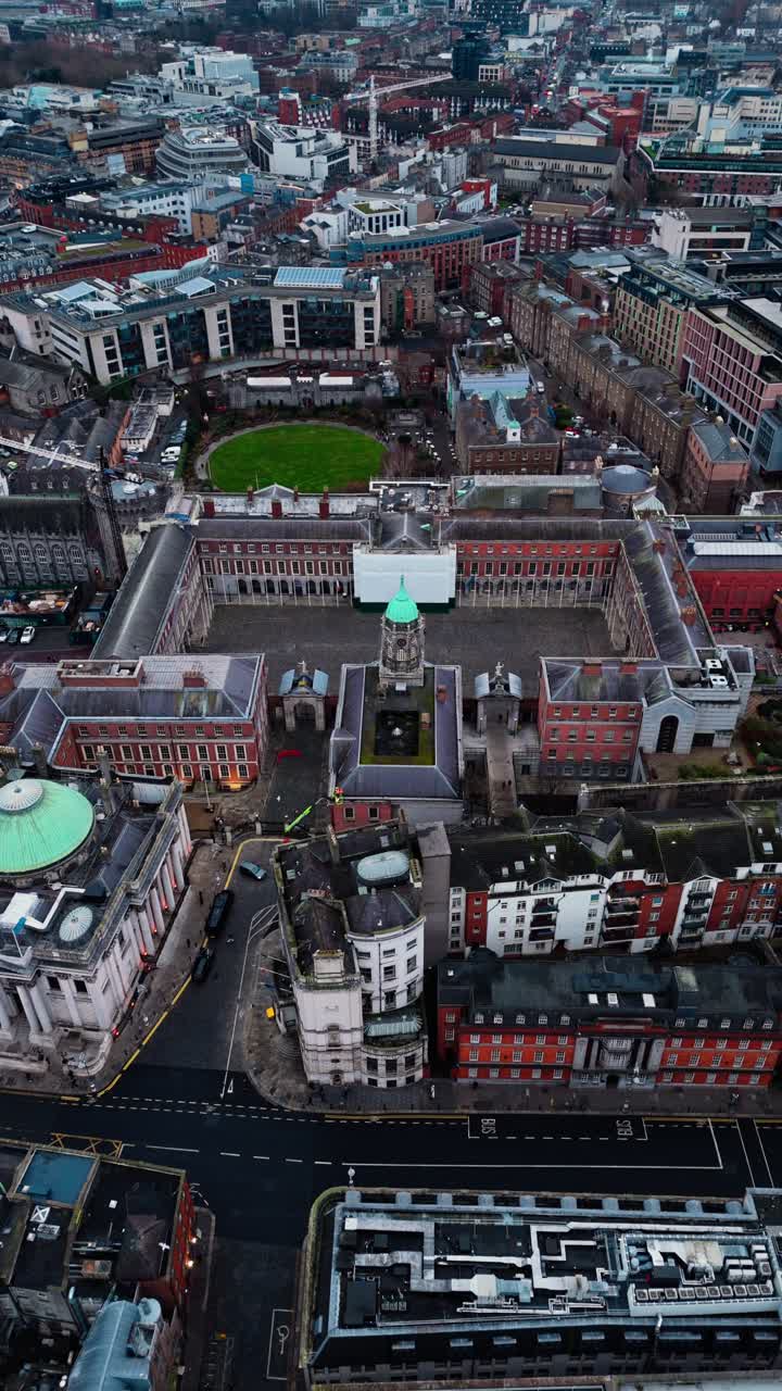 Drone shot over Dublin castle in the city centre in Ireland with busy streets below with cars and buses and tourists walking around in Irish cityscape on cloudy overcast day in winter