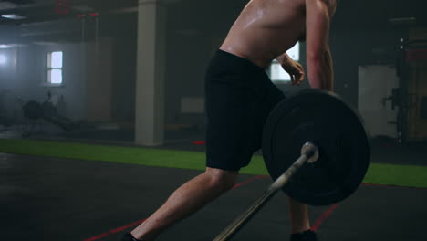 the boy pushes the barbell in the gym with one hand. an athlete without a t-shirt in a dark room lifts the barbell while practicing the force of the impact