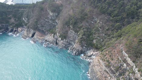 drone aerial view in south korea countryside flying over the clear blue sea of busan next to a green mountain on a sunny day top view