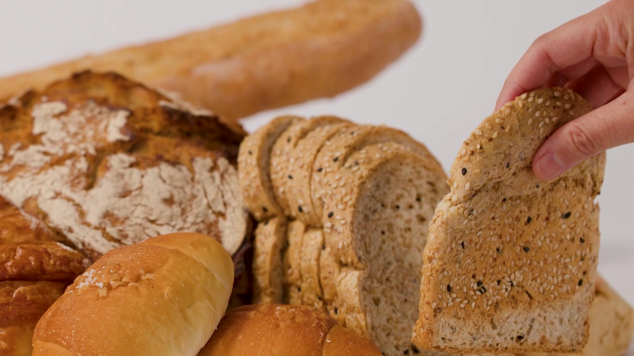 Close-up shot of hands selecting sliced multigrain bread from a variety of fresh baked loaves.