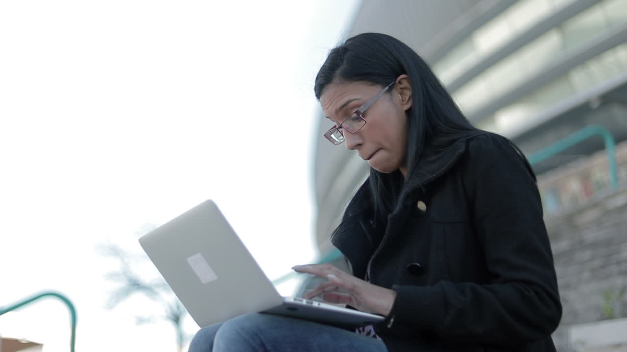 Smiling hindu woman in eyeglasses typing on laptop outdoor