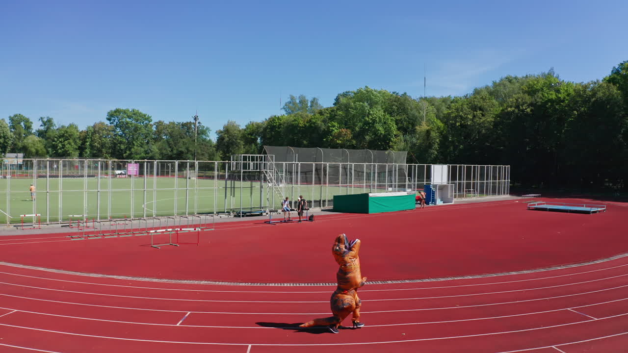 Dinosaur Tirex running along the track at the stadium. Air inflatable costume of dinosaur outdoors on sunny summer day.