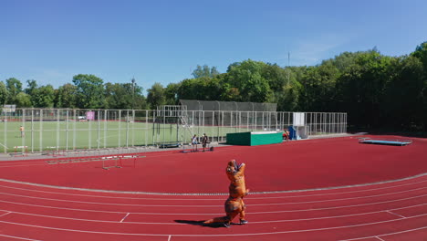 dinosaur tirex running along the track at the stadium. air inflatable costume of dinosaur outdoors on sunny summer day.
