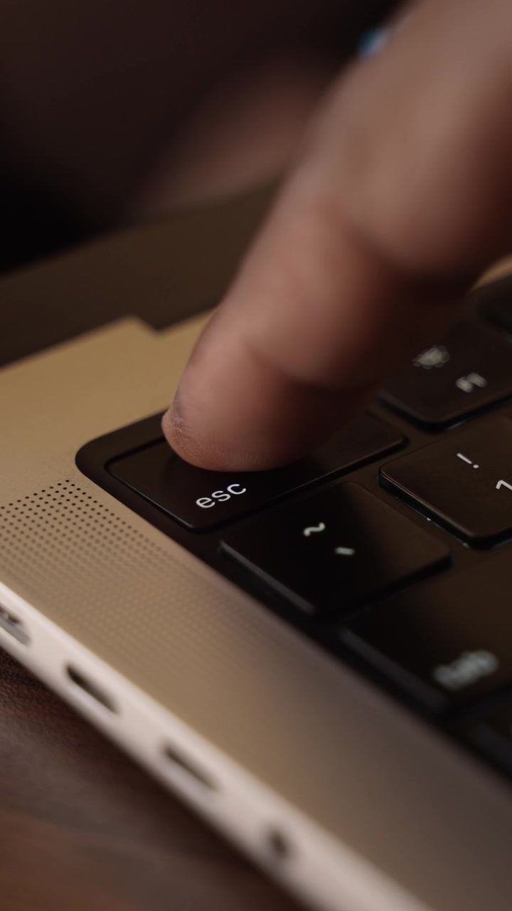 Dedo presionando la tecla Escape en el teclado de un portátil en una habitación con luz cálida