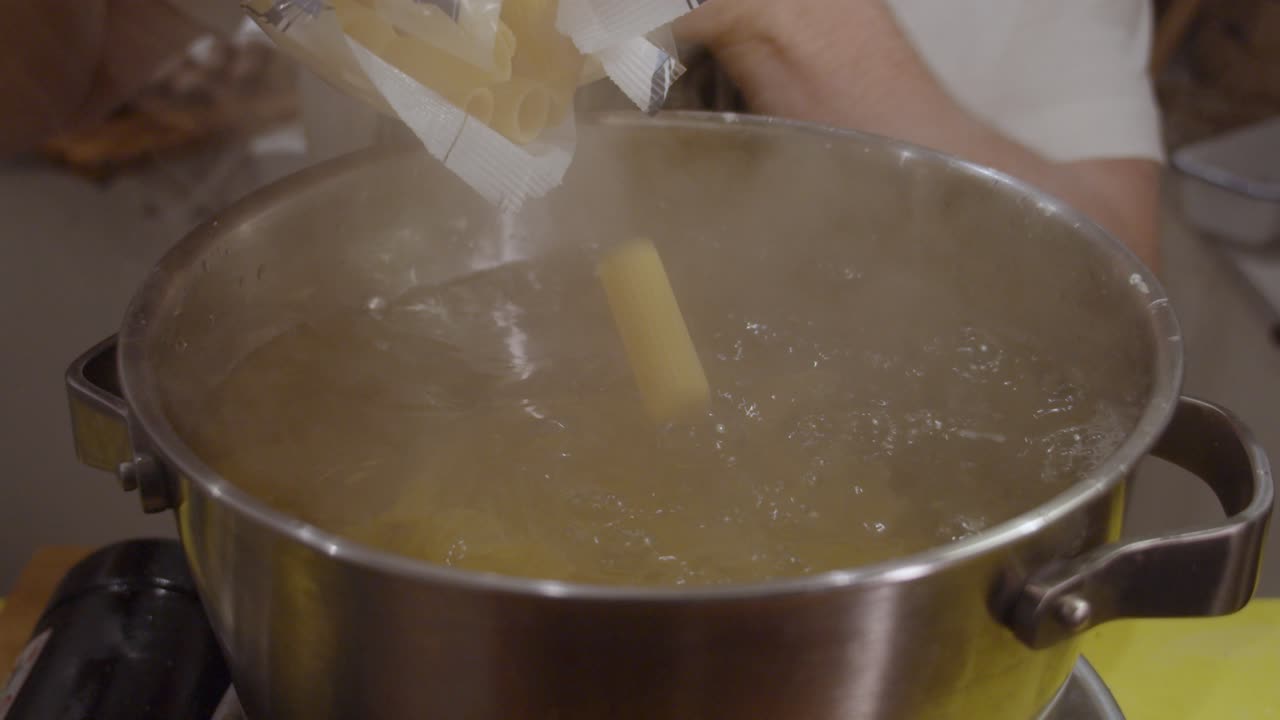 Pasta che cade dalla confezione nella pentola con acqua bollente.