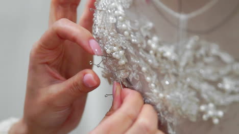 Close-up-fashion-designer-for-brides-in-his-Studio-pins-needles-lace-wedding-dress.-Seamstress-creates-an-exclusive-wedding-dress.-Secure-with-pins-and-needles-outline.-Small-private-business.-Sew-rhinestones-and-crystals-to-the-dress-thread-and-needle.-Jewelry-work.