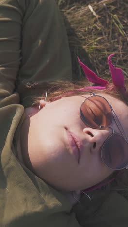 pretty plump young lady in sunglasses sleeps on dry grass at campsite in autumn evening close view