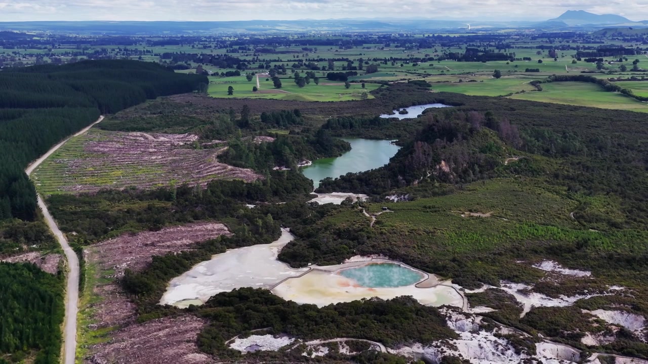 Vista aérea de uma paisagem geotérmica perto de Rotorua, com um rio sinuoso, áreas minerais coloridas, plantações florestais e terras agrícolas abertas criando uma paisagem vulcânica distinta da Nova Zelândia