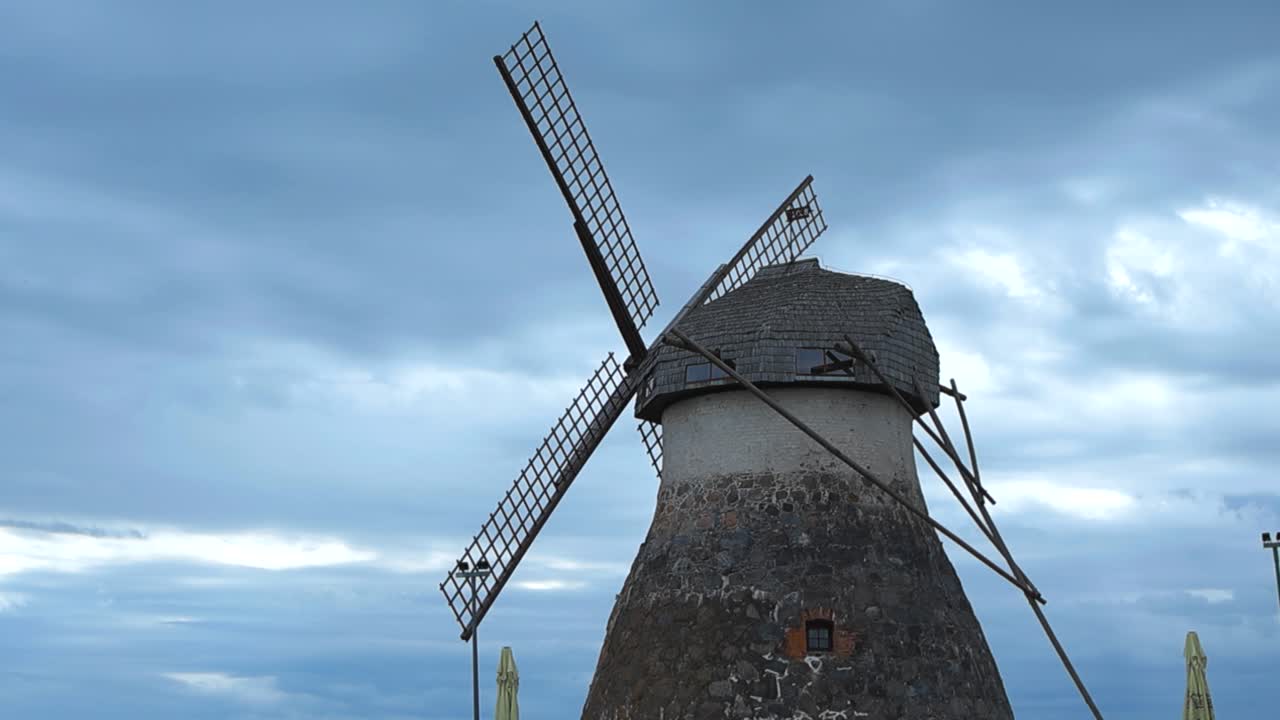 Low angle wide shot of a old historic stone windmill with large wooden blades or wings during a cloudy day in Kuremaa. national heritage site is protected and renovated. Blue and white clouds visible