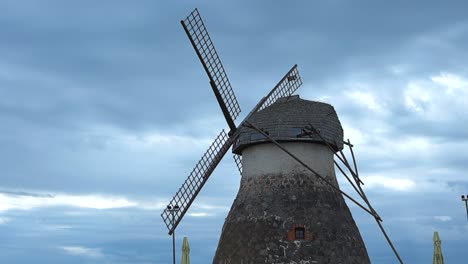 low angle wide shot of a old historic stone windmill with large wooden blades or wings during a cloudy day in kuremaa. national heritage site is protected and renovated. blue and white clouds visible
