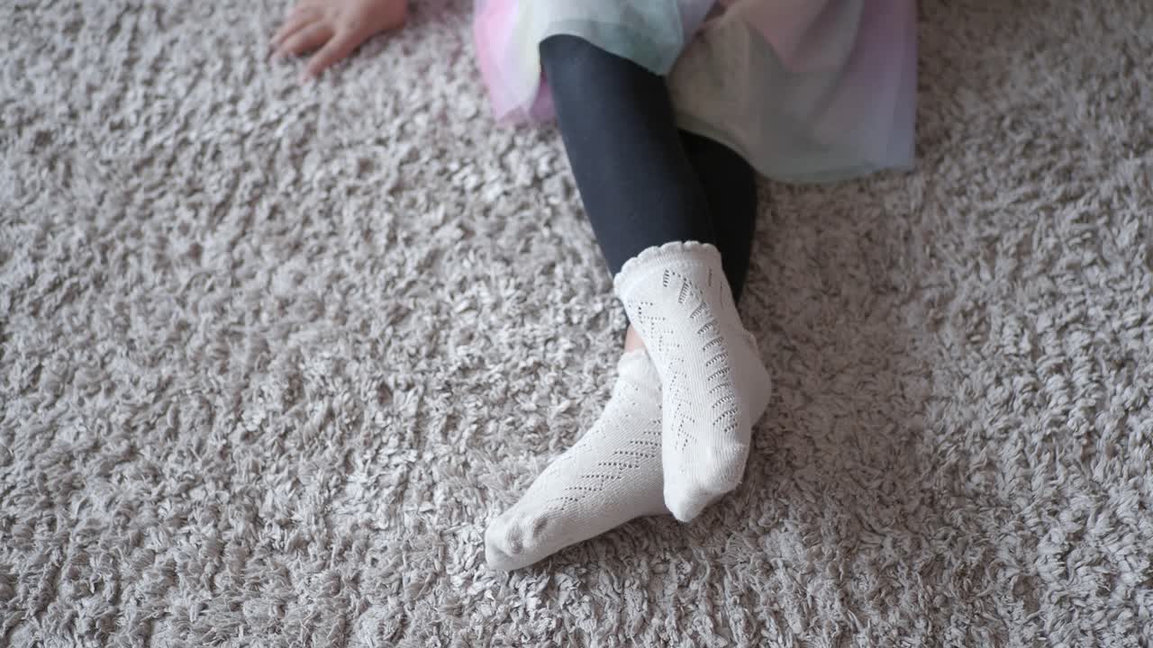 una niña adorable con calcetines blancos sentada en una alfombra peluda beige