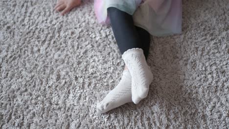 adorable little girl wearing white socks sitting on a beige shaggy carpet