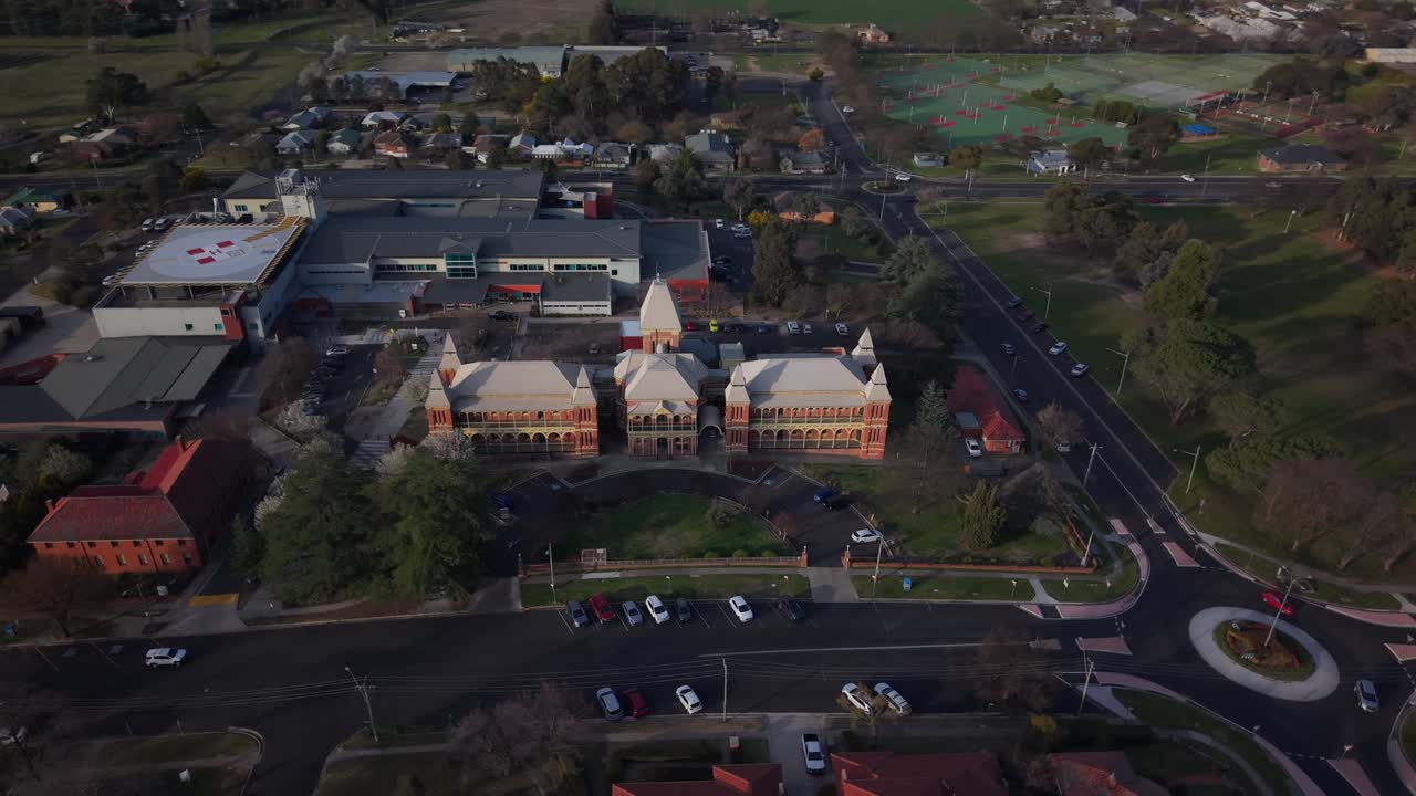 Hospital and streets glowing with sunset light as drone glides above residential Bathurst area, aerial angled establish, NSW Australia