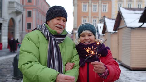 senior couple with burning sparklers bengal lights celebrating anniversary, making a kiss on street