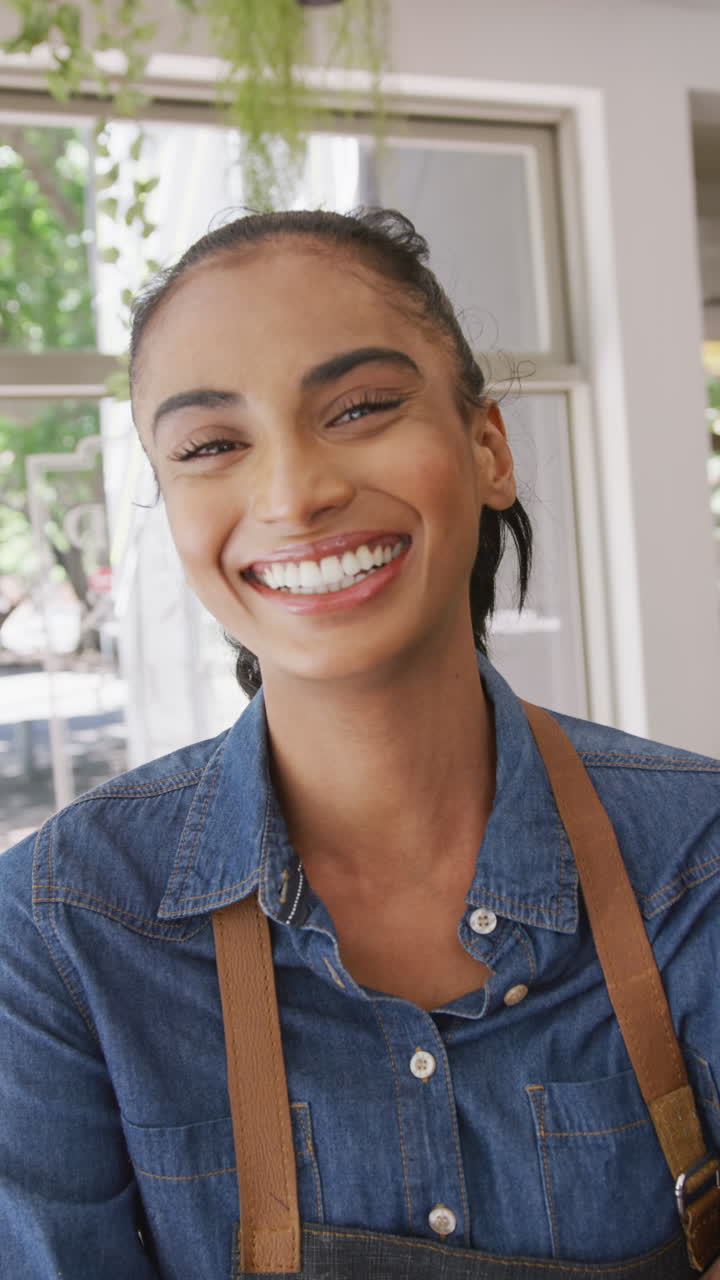 Vertical video of portrait of happy biracial female barista in her cafe shop