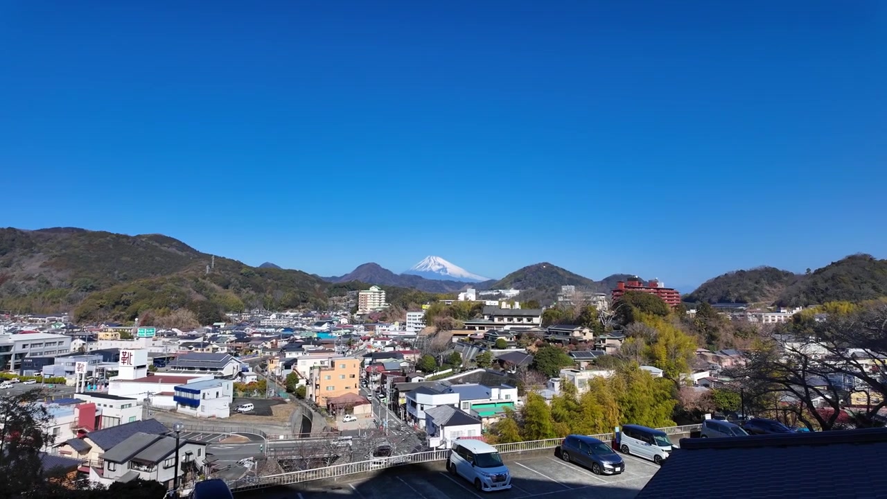 Ampia vista panoramica della città di Izu-Nagaoka annidata in una valle con la cima innevata del Monte Fuji in lontananza.