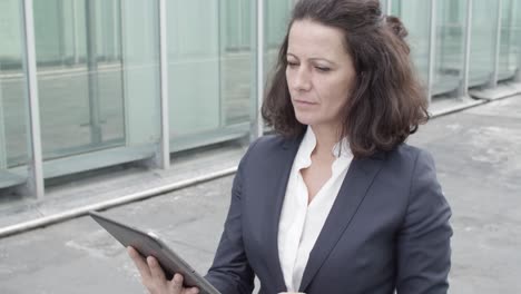 dolly shot of a focused businesswoman in suit using tablet for work while walking outside