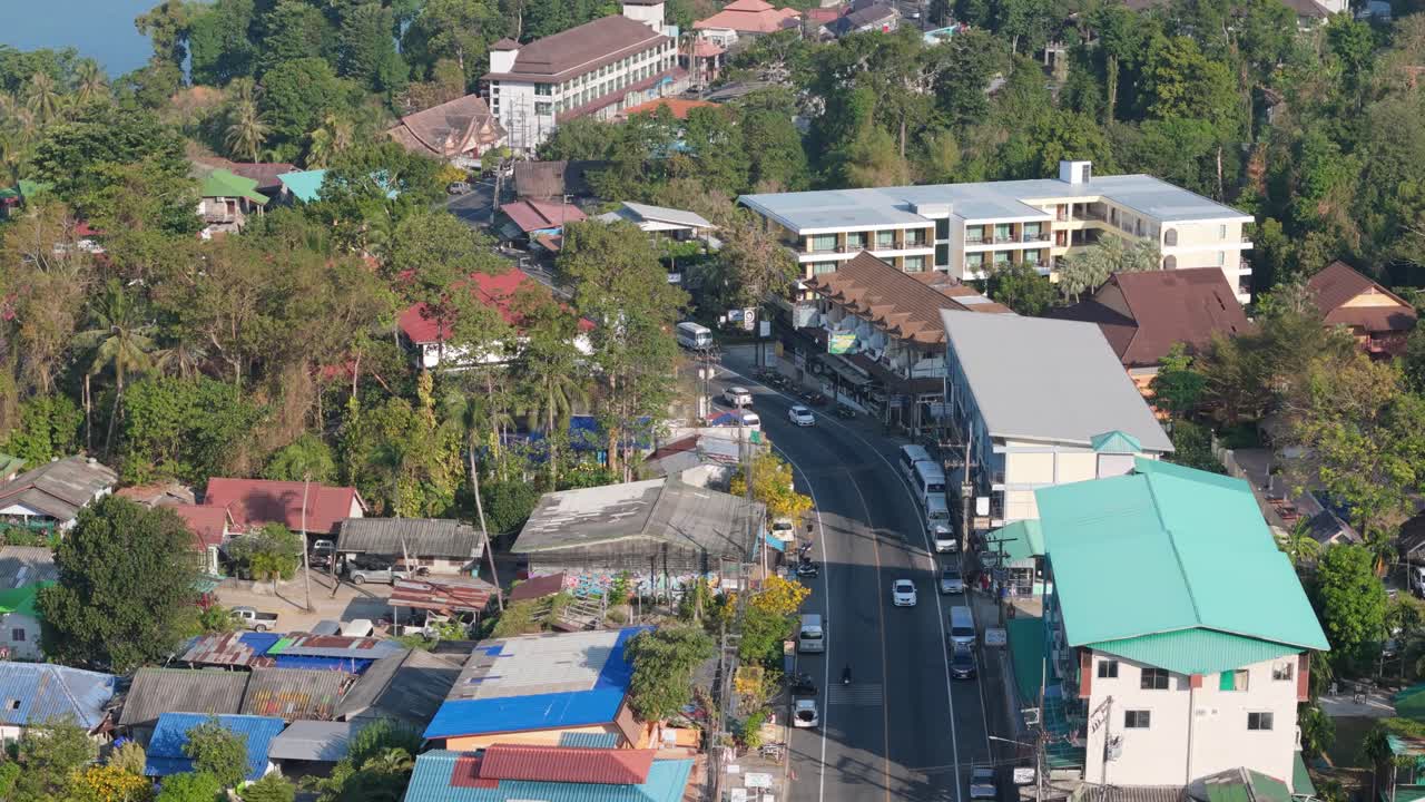 Flyover drone shot of Koh Chang's White Sand Beach, Thailand. Sunny morning over the village, sea, and lush greenery