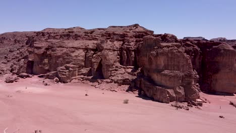 Aerial-slow-and-calming-forward-drone-shot-of-a-ridge-in-the-middle-of-a-desert,-surrounded-by-boulders,-sand-and-dirt