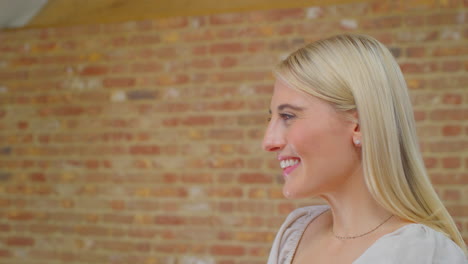 Young-Woman-Standing-By-Brick-Wall-At-Home-Talking-And-Laughing-With-Person-Off-Camera