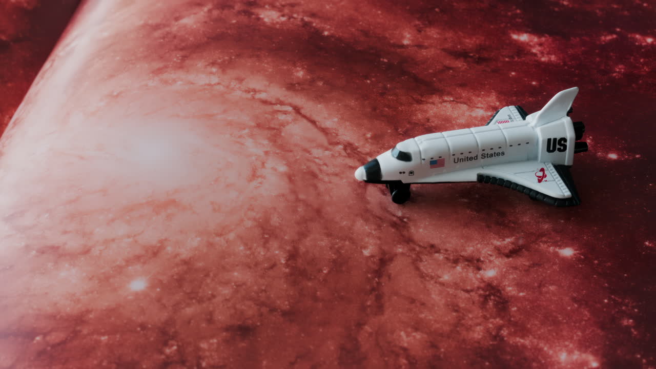 Close up of a miniature toy space shuttle placed on a reddish galaxy background