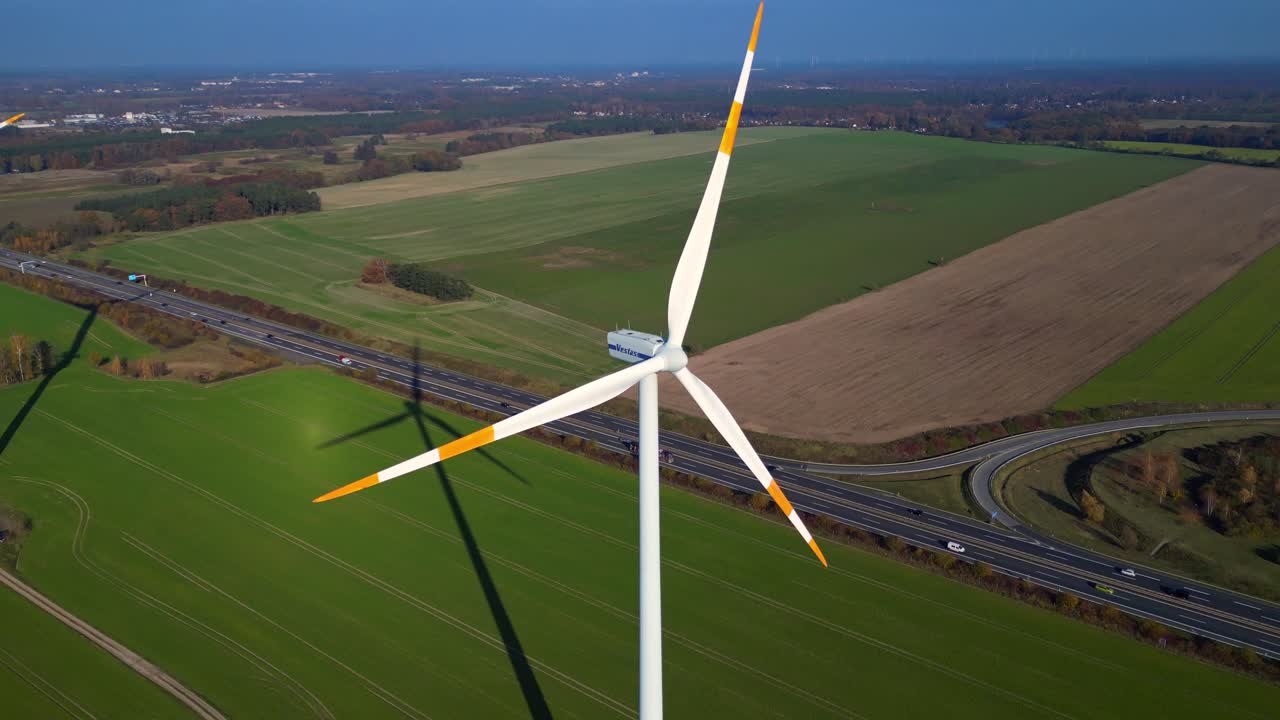 Wind turbine standing in green field next to highway autobahn in autumn Germany, generating renewable energy. Dramatic aerial view flight drone top down Above view