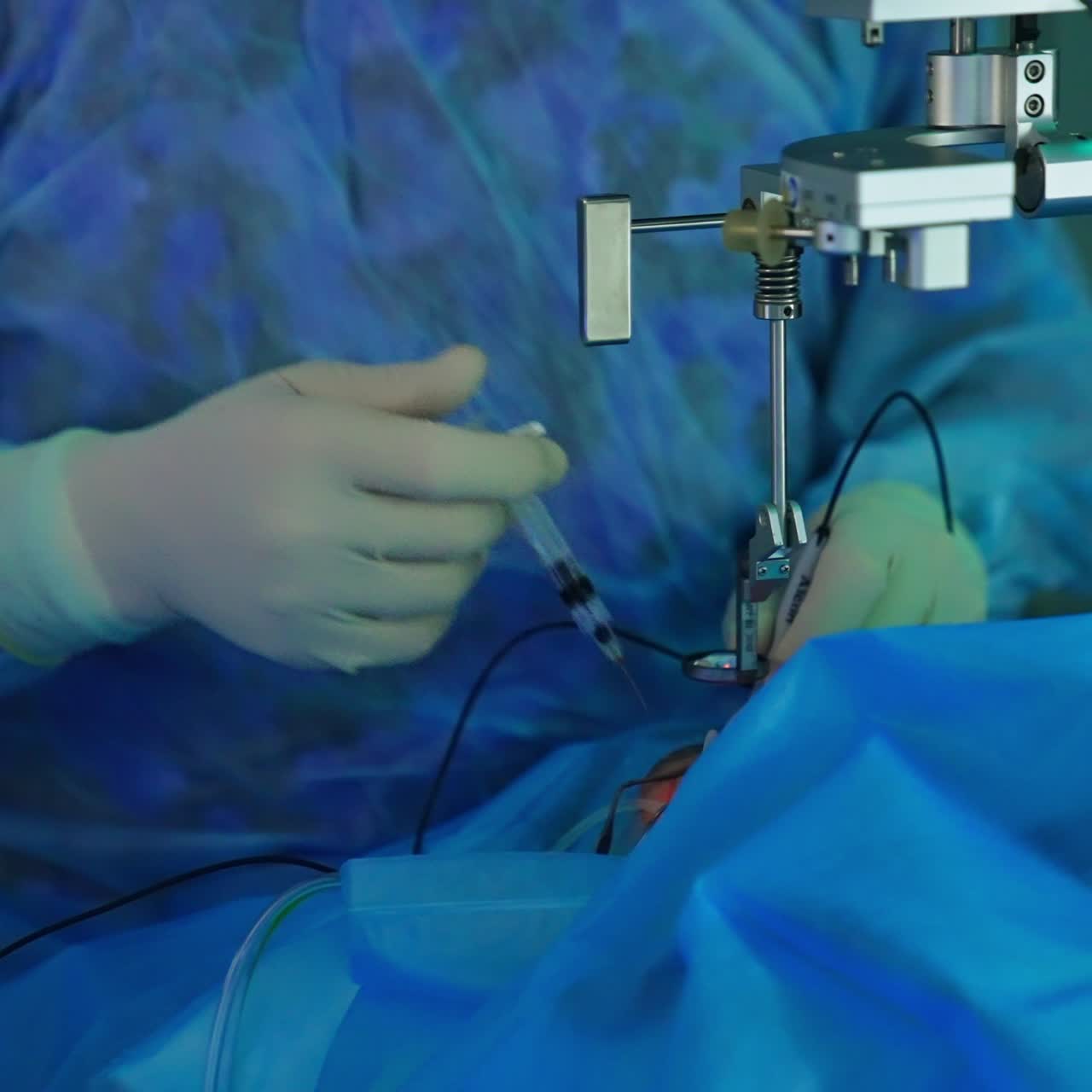 Surgeon's hand in gloves input medicines into patient's eye from a syringe. Doctor holds the device with red light in the other hand