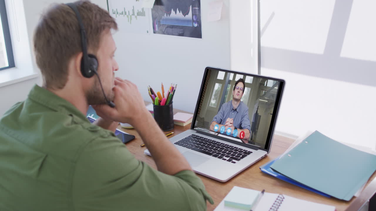 Kaukasisk mand bruger bærbar computer og telefonheadset på videoopkald med en mandlig kollega.