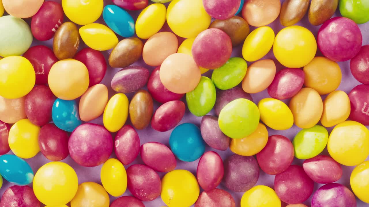 Colorful dragee candies lollipops with glitter sprinkles on purple background. Summer bright texture studio shot for store, supermarket, close-up top view, zoom. Children sweets made of sugar.