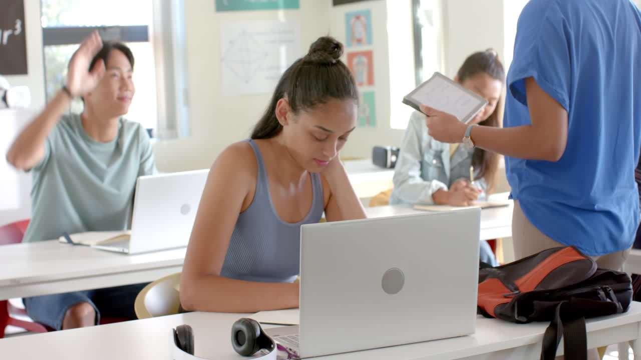 In high school, students using laptops and tablets in classroom, focusing on studies