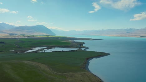 Scenic-aerial-landscape-view-of-beautiful,-remote-Lake-Tekapo-surrounded-by-mountainous-terrain-in-Mackenzie-Basin-of-Canterbury,-New-Zealand-Aotearoa