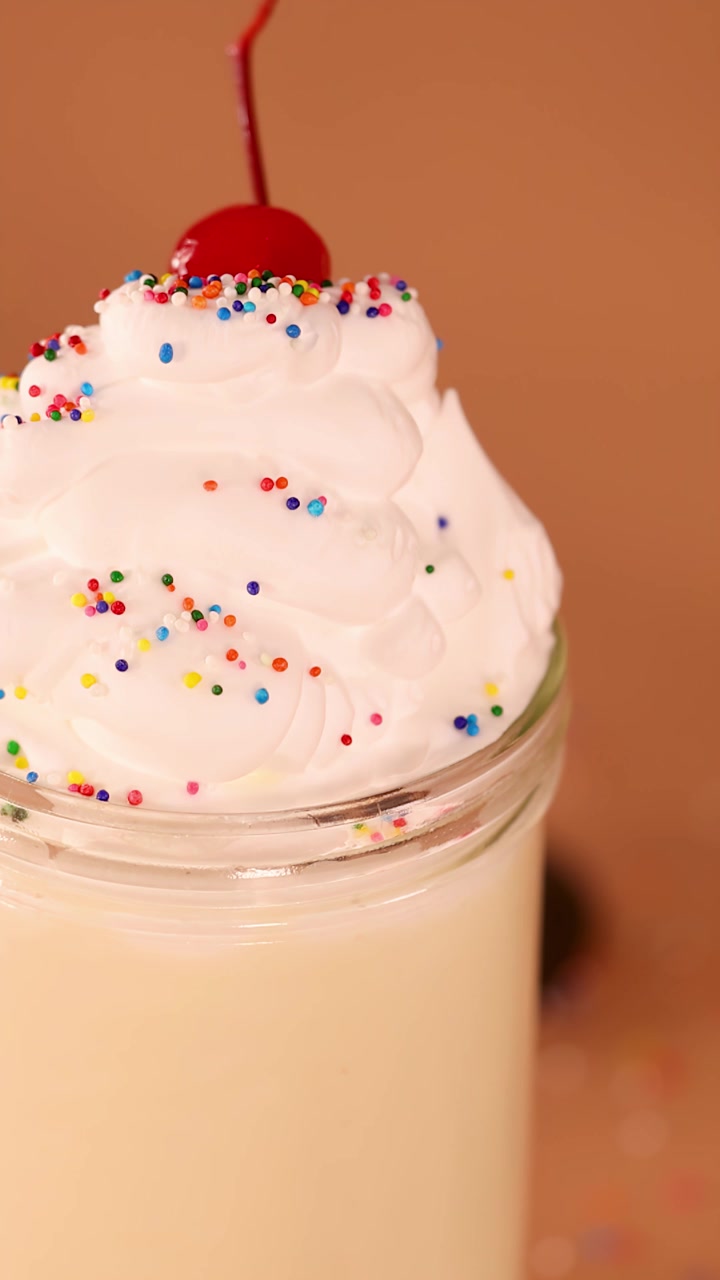 Primo piano lento di un milkshake cremoso alla vaniglia con panna montata, codette colorate e guarnizione di ciliegia