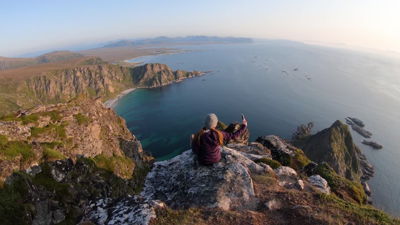 한 젊은 여성이 노르웨이 베스테랄렌에 있는 마틴덴 산의 가파른 절벽 가장자리에 혼자 앉아 있습니다.