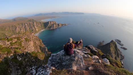 A-young-woman-sits-by-herself-on-the-edge-of-a-steep-cliff-on-Måtinden-mountain-in-Vesterålen,-Norway