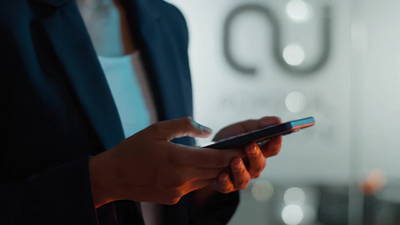 A Professional Individual Engaged in Texting or Communicating via Smartphone in a Dimly Lit Environment with Abstract Background Elements Highlighting Modernity