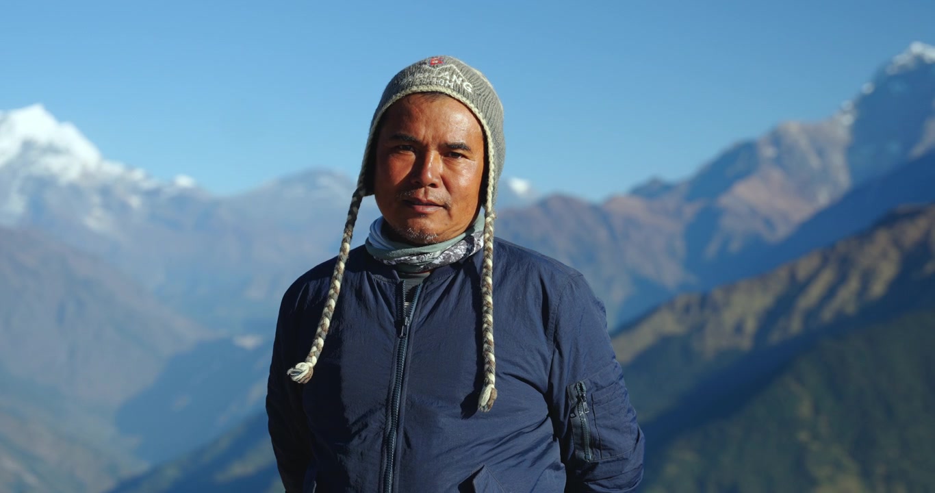 Annapurnan alue, Nepal, lähikuva paikallisesta etniseen gurung-heimoon kuuluvasta Himalajan kantajaoppaasta, jolla on yllään villapipo, Annapurna Southin seisoessa taustalla