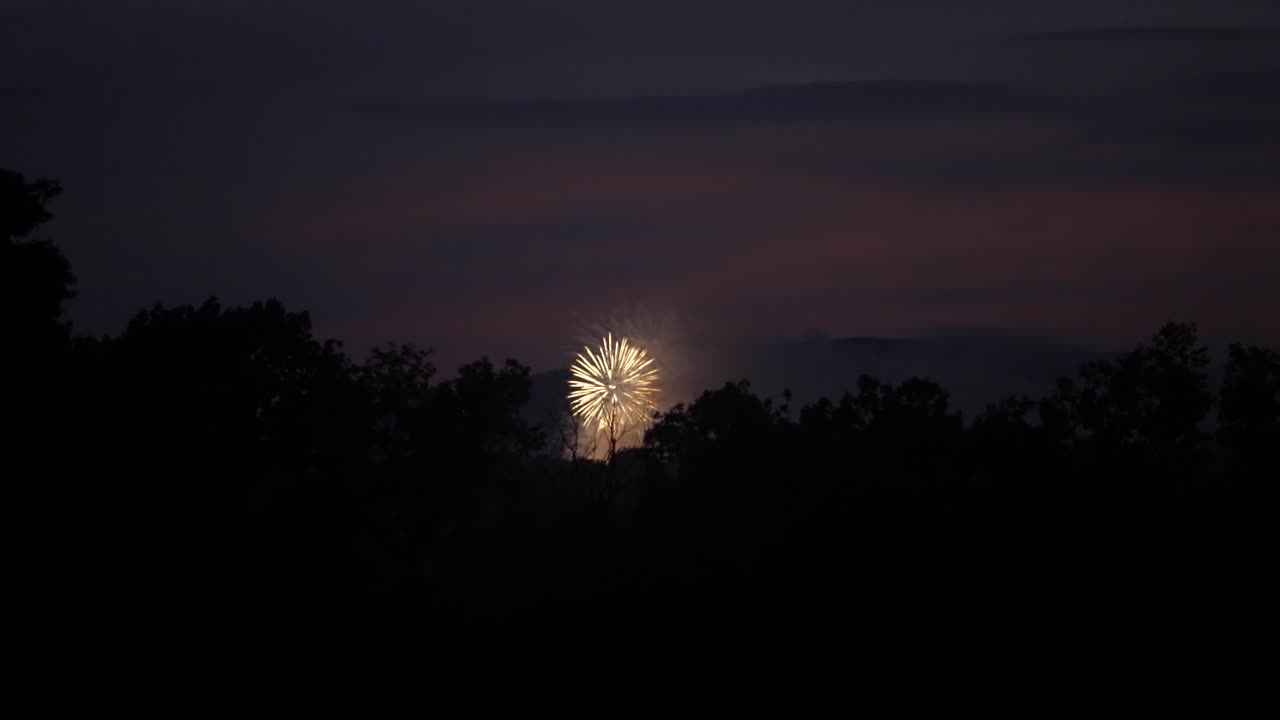 los fuegos artificiales estallan y explotan extendiendo un resplandor amarillo a naranja en cámara lenta por la noche