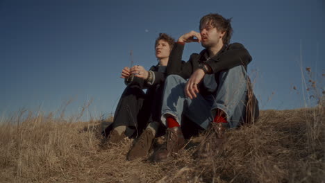 couple sitting on hillside beneath clear blue sky and talking