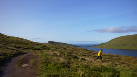 Man-opens-his-arms-happily,-jumps-from-rock-running-towards-Lake-Sorvagsvatn