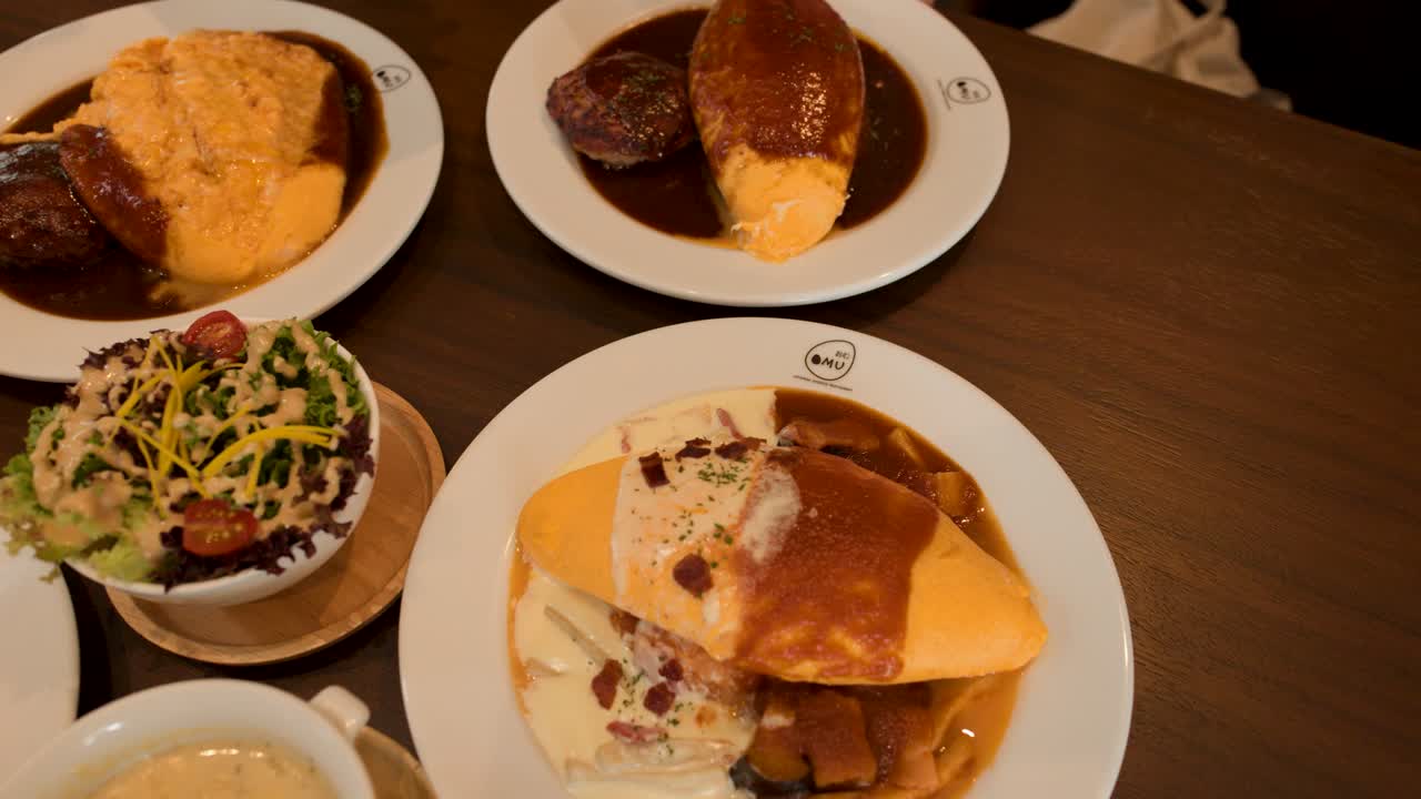 Overhead view of Japanese omelette rice, salad, soup, and sides on restaurant table, warm lighting