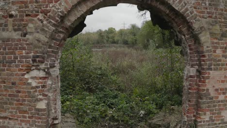 flying through derelict building archway with green foliage behind