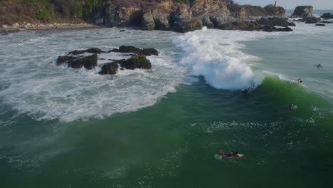 Surfers-surfing-next-to-rocks,-over-Rough-sea-with-waves,-Close-Aerial-shot