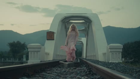 woman in pink lace dress walking on railway tracks bridge