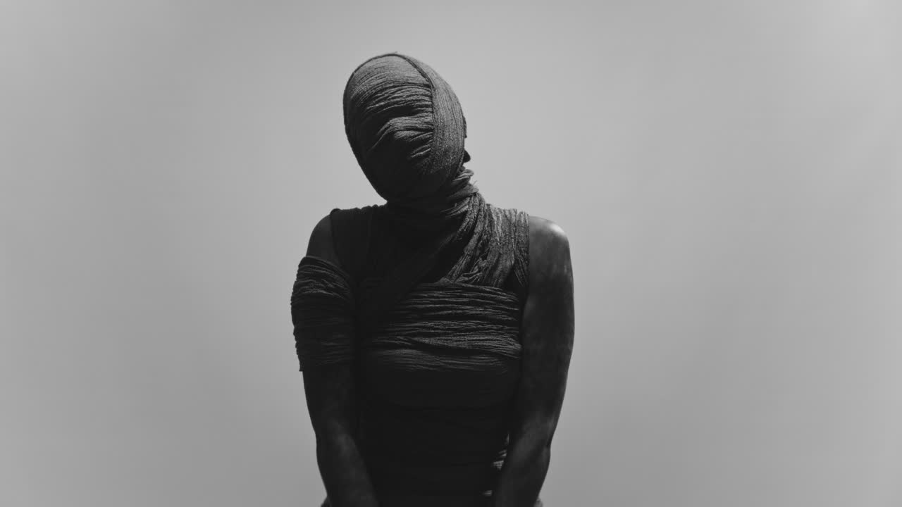 A mummy of a woman on a white backdrop slowly turns her head
