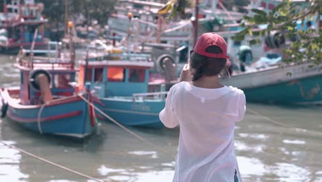 girl-with-phone-in-pictorial-bay-with-fishing-boats-on-day