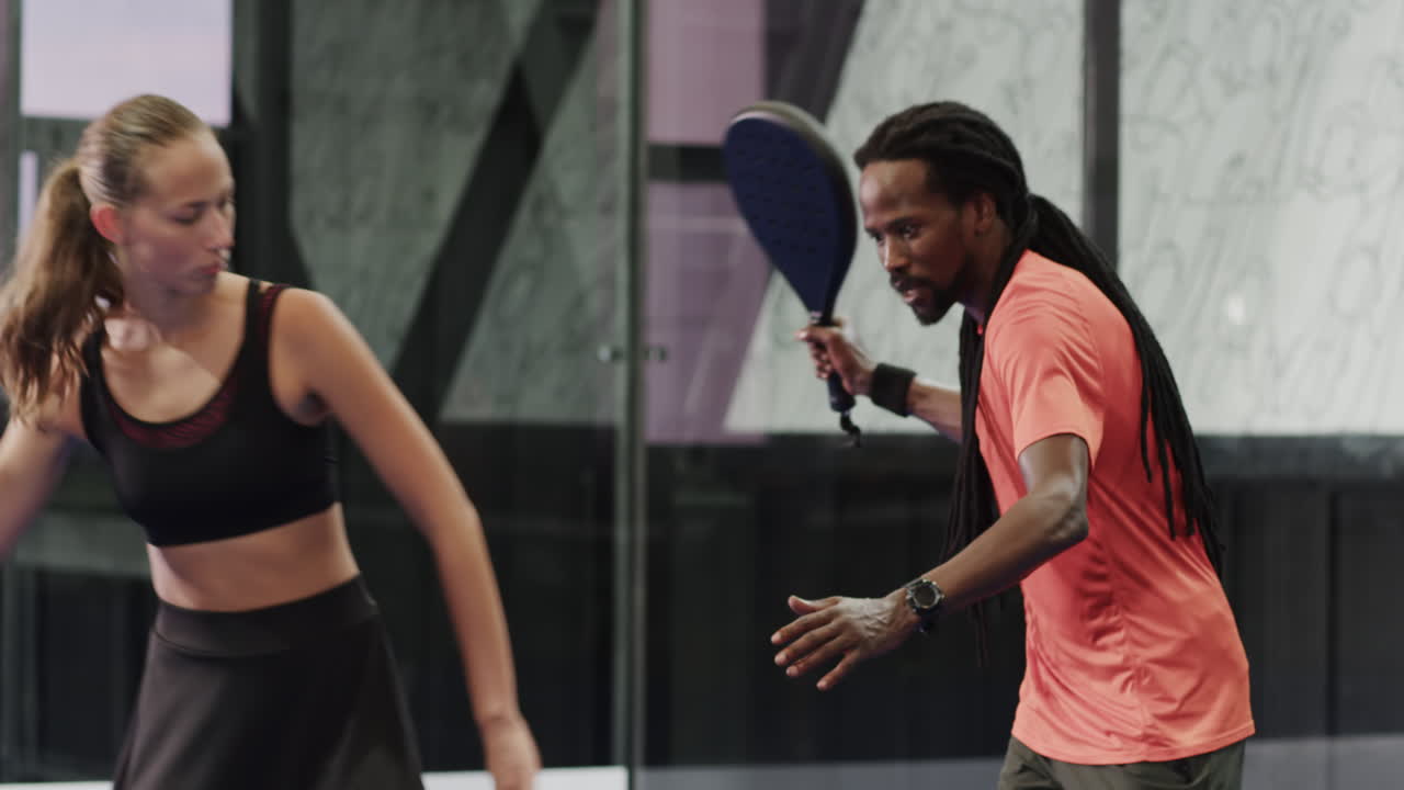 Smiling man and woman playing padel tennis on indoor court, enjoying friendly match