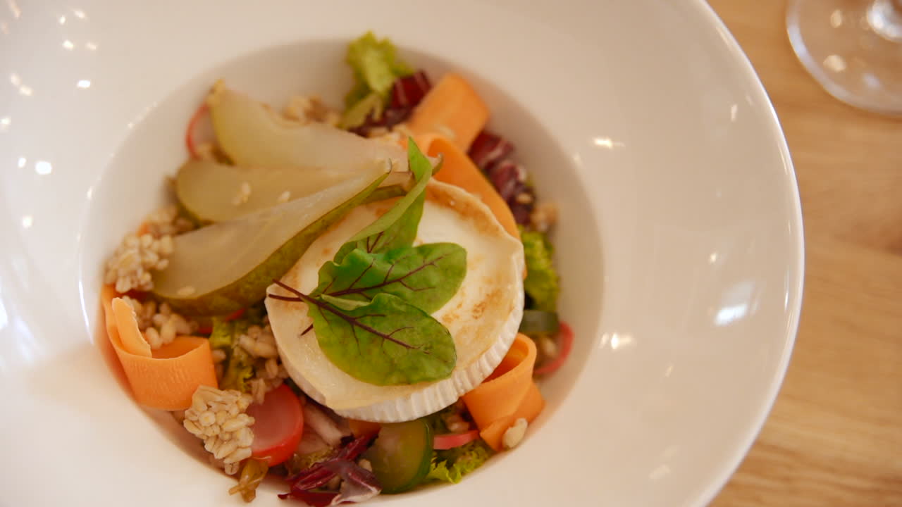 Fancy gourmet salad with grilled cheese, fresh pear and vegetable ribbons, served in a white bowl. Close up gimbal of a healthy and elegant meal.