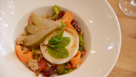 fancy gourmet salad with grilled cheese, fresh pear and vegetable ribbons, served in a white bowl. close up gimbal of a healthy and elegant meal.