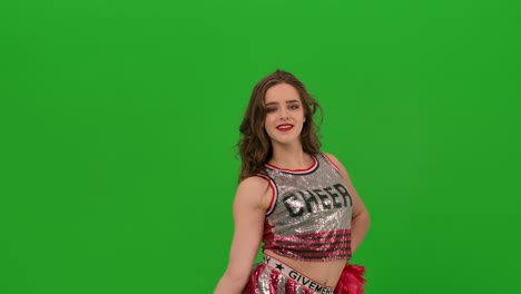 una adorable animadora en uniforme con pom-poms rojos realiza un baile jubiloso. retrato de una joven mujer sonriente bailando en el estudio en una pantalla verde. primer plano. cámara lenta